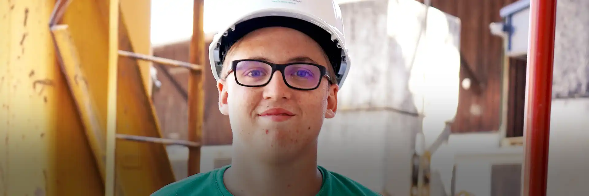 Lächelnder Praktikant mit Bauhelm auf einer Baustelle