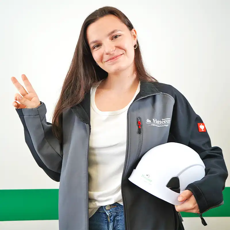 Eine l&auml;chelnde Praktikantin mit Helm unterm Arm, die das "Peace" Zeichen mit der Hand formt